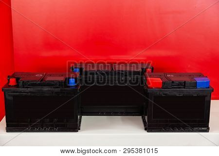 Three New Black Rechargeable Batteries For Car And Vehicle Stand  On A Red Background With White Ins