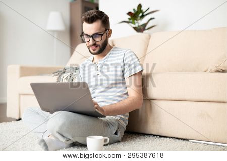 Young busy home office manager or freelancer in casualwear looking at laptop display while doing remote work