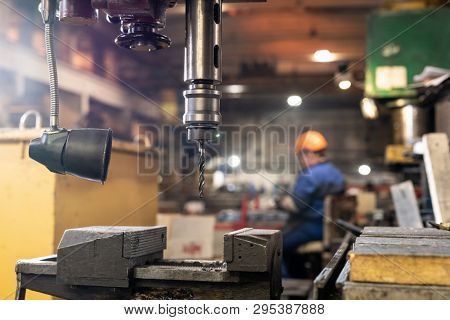 Part of metallic drilling machine hanging over workpiece or element of industrial equipment during working process