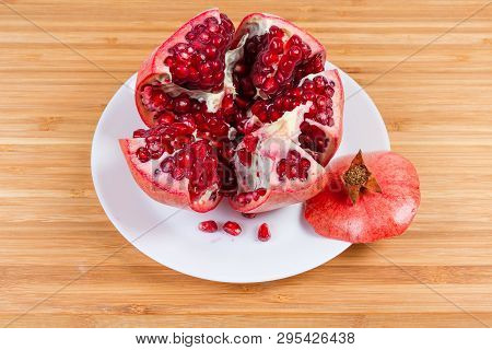 Open Thru Split Ripe Pomegranate Fruit And Several Fallen Out Seeds On The White Dish On A Bamboo Wo