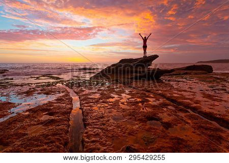 Female Standing On Top Of Shark Rock On The Coastal Rock Shelf Admiring The Magnificent Sunrise Whic