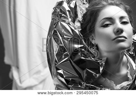 Arty Portrait Of A Fashionable Queen-like Model With Silver Foil Cape Over White Curtain Background.