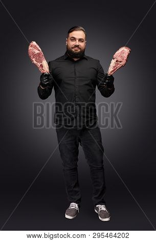 Handsome Bearded Meatman In Stylish Outfit Holding Pieces Of Raw Meat And Looking At Camera