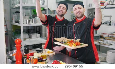 Restaurant Kitchen. Two Men Chefs Finished Serving Dishes With A Bellissimo Gesture