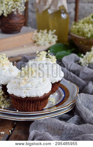 Chocolate Capcakes With Vanilla Cream Sprinkled With White Chocolate And Elderberry Flowers. Vintage