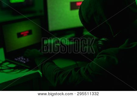 Unrecognizable Man In Hoodie Using Laptop To Extort Money Through Internet While Sitting In Room Wit