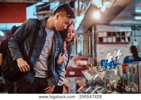 Romantic Asian Couple Looking For Something Special At Seafood Chainese Market. They Are Curious And