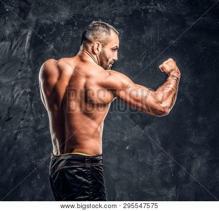Professional Fighter Showing Kick Fighting Technique. Studio Photo Against A Dark Textured Wall