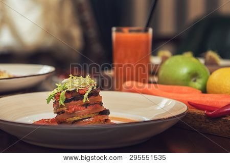 Healthy vegeterian food on brown wood board. Baked vegetables in layers, fruits and carrot juice