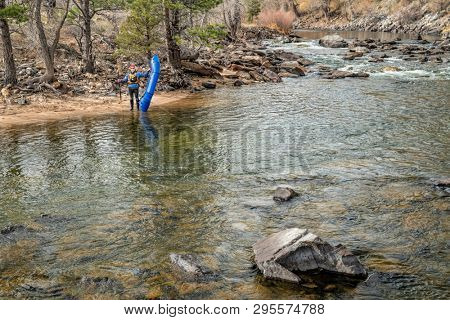 senior paddler with an inflatable packraft on a shore of mountain river in early spring - Poudre River above Fort Collins, Colorado
