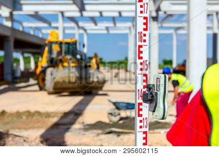 Construction Worker Is Holding Leveling Rod To Help Surveyor, Geodesist To Measure Position, Depth.
