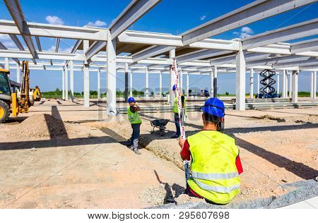 Construction Worker Is Holding Leveling Rod To Help Surveyor, Geodesist To Measure Position, Depth.
