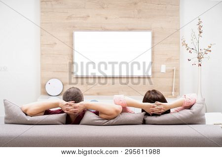 Back View Of Couple Man And Woman Resting In Apartment, Sitting On Sofa Together And Watching Tv