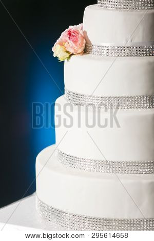 A Four-tiered Cake With White Cream Silver Rhinestones And Live Roses Stands On A Blue Background