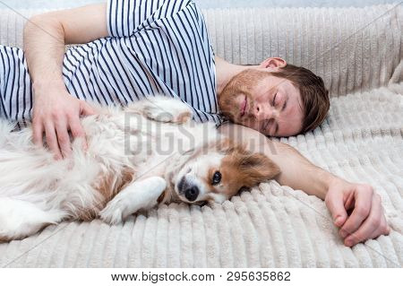 Portrait Of A Young Man Sleeping With His Dog In An Embrace On The Bed
