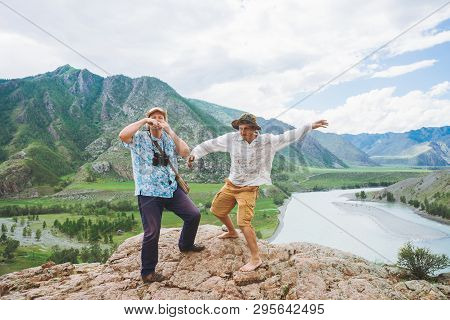 Two Joyous Crazy Tourists In Hats On Rock Against Valley Among Mountain River And Giant Mountains. P
