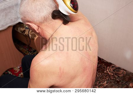 An Old Man With Gray Hair Doing His Own Neck Massage With An Electric Massager At Home. Restoration 