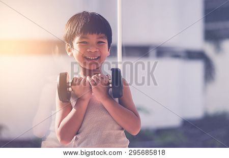 Little Boy Is Working Out With Dumbbell By The Windows City.