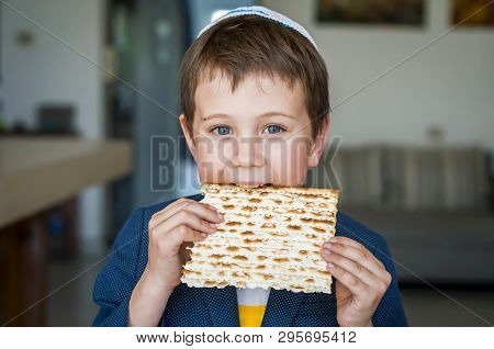Cute Caucasian Jewish Boy Holding In His Hands And Taking A Bite From A Traditional Jewish Matzo Unl