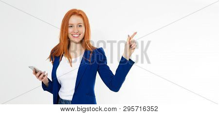 Pretty Redhead Girl With Phone Smiling Pointing Finger Right On White Background. Young Foxy Female
