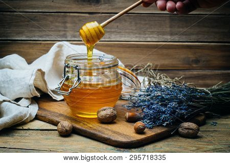 Honey In A Jar With Wooden Honey Dipper On A Wooden Board With Crackers, Nuts And Lavender Flowers