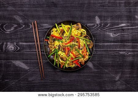 Appetizing Stir Fried Noodles With Garlic Sprouts, Mushrooms, Red Pepper And Chicken Meat On A Black