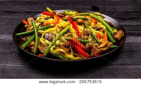 Appetizing Stir Fried Noodles With Garlic Sprouts, Mushrooms, Red Pepper And Chicken Meat On A Black