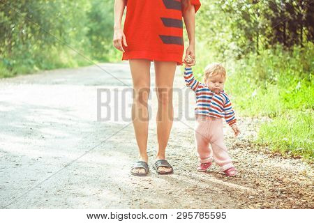 The Child Learns To Walk In The Park Barefoot On The Grass