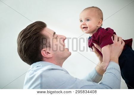 Father Lifting Smiling Baby Son Into Air At Home As They Play Gane Together