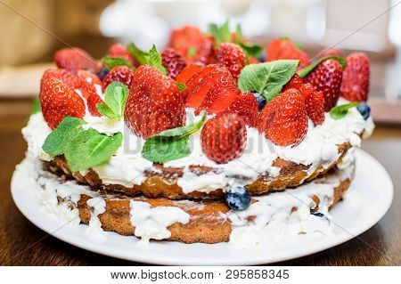 Strawberry Cake In Cream And Mint Leaves On The Table In A Plate, On The Background Of A Teapot With