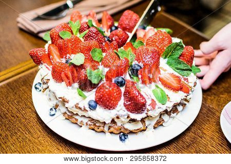 Strawberry Cake With Blueberries In Cream And Mint Leaves In The Process Of Cutting Into Pieces On A