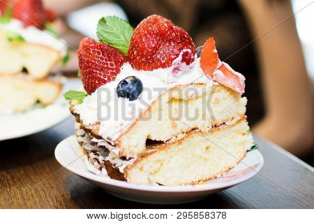A Piece Of Cake With Strawberries In Cream, Blueberries And Mint Leaves, On A Plate, In Light Colors