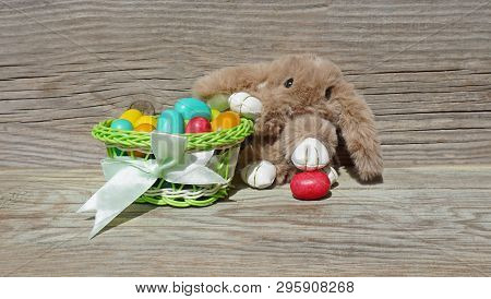 Easter Bunny With A Basket Of Colorful Easter Eggs On A Wooden Background. Easter Postacard. Seasona
