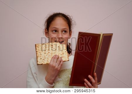 Portrait Of The Cute Teenager Girl Holding Matzah And Reads The Passover Haggadah. Jewish Child Eati