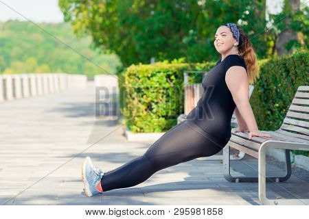 Portrait Of Active Happy Plump Woman Performs Exercises In The Park On A Bench