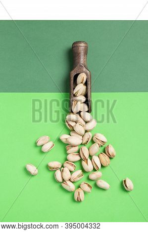 Flat Lay Composition. Pistachios On Wooden Spoon On Green Background. Vertical Format.