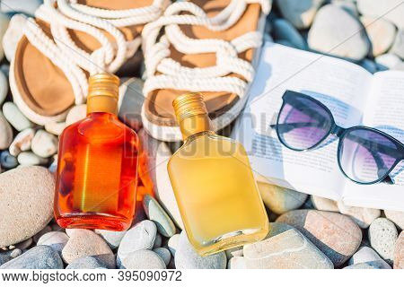Beach Hat On Opened Book With Sunscreen And Shoes On Pebble Beach