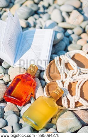 Beach Hat On Opened Book With Sunscreen And Shoes On Pebble Beach