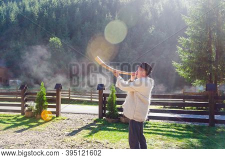 A Man In Traditional Hutsul Clothing Plays The Trembita Horn In The Sunlight.