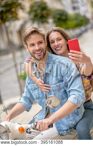 Woman Taking Picture With Her Boyfriend Ridig A Scooter
