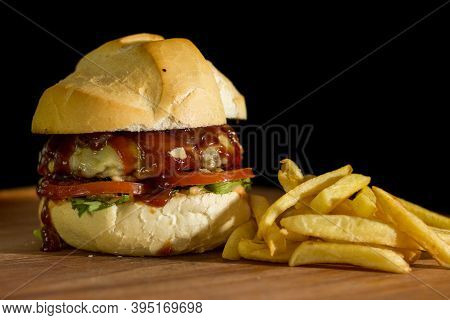 Close Up Of A Homemade Burger With Barbecue Sauce On A Chopping Wood Board, On Black Background