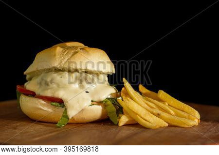 Close Up Of A Homemade Burger With Extra Cheese On A Chopping Wood Board, On Black Background