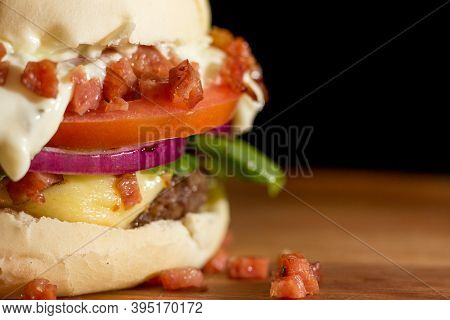 Close Up Of A Homemade Burger With Bacon And Salad A Chopping Wood Board, On Black Background