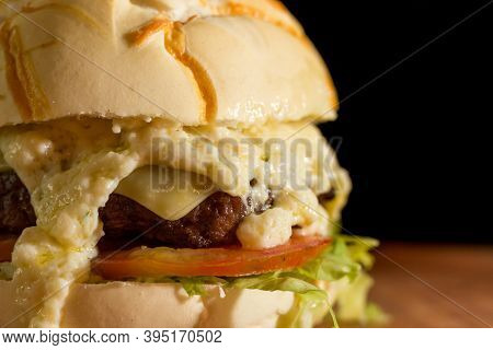 Close Up Of A Homemade Burger With Extra Cheese On A Chopping Wood Board, On Black Background