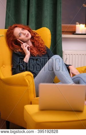 Nice beautiful lady with redhead curly hair work at the notebook sit down on the sofa at home - check on oline shops for cyber monday sales - technology woman concept for alternative office freelance