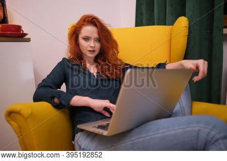 Nice beautiful lady with redhead curly hair work at the notebook sit down on the sofa at home - check on oline shops for cyber monday sales - technology woman concept for alternative office freelance