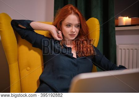 Nice beautiful lady with redhead curly hair work at the notebook sit down on the sofa at home - check on oline shops for cyber monday sales - technology woman concept for alternative office freelance