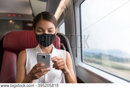 Asian business woman using mobile phone during commute to work in public transport train wearing face mask for corona virus prevention.