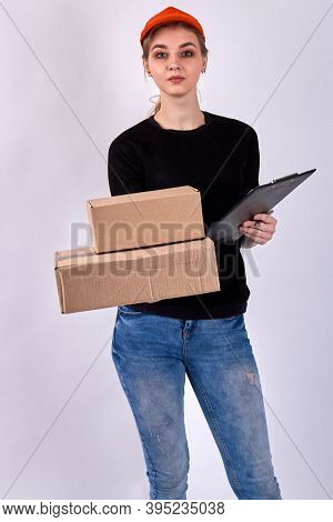 Pretty Courier Girl Is Holding Cardboard Parcels. Caucasian Female In Jeans And Black Sweater With C