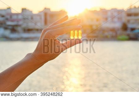 Yellow Gel Capsule Vitamin D Omega-3 In Womans Hand, Sun Sea Background.